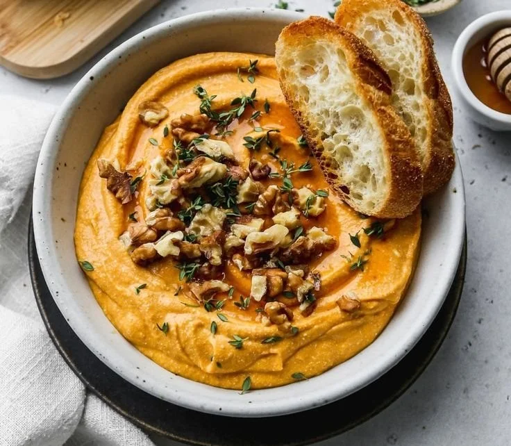A bowl of Pumpkin Whipped Feta Dip garnished with herbs and served with crackers.