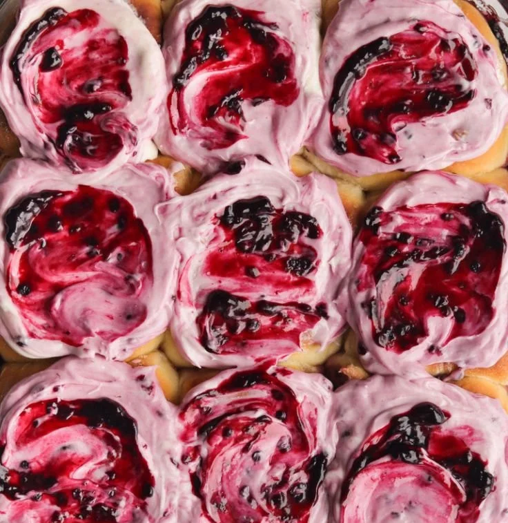 Freshly baked blackberry cinnamon rolls with icing on a plate