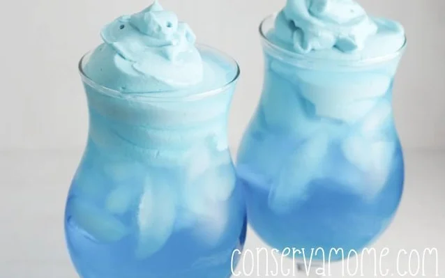 A vibrant glass of whipped Kool Aid topped with whipped cream and colorful sprinkles.