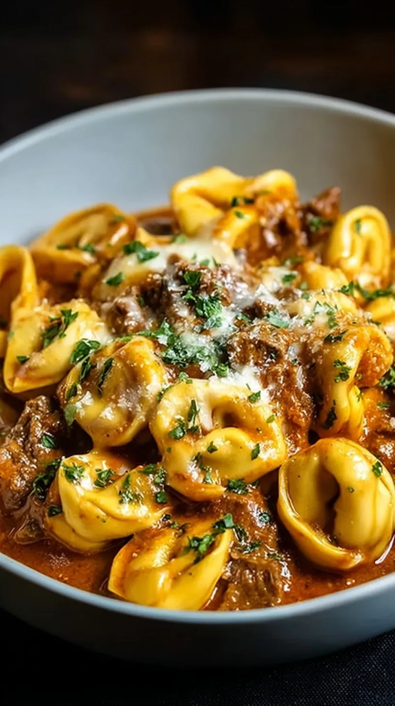 A bowl of creamy cheesesteak tortellini with bell peppers and onions in a provolone sauce.