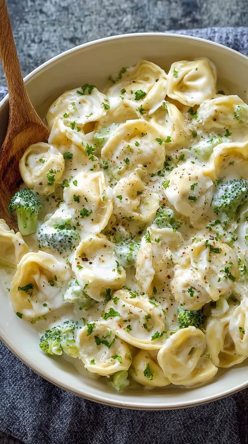 A bowl of cheese tortellini coated in a thick, white Alfredo sauce and topped with fresh green parsley.